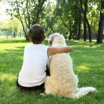 Boy and Dog Sitting in Grass from Back